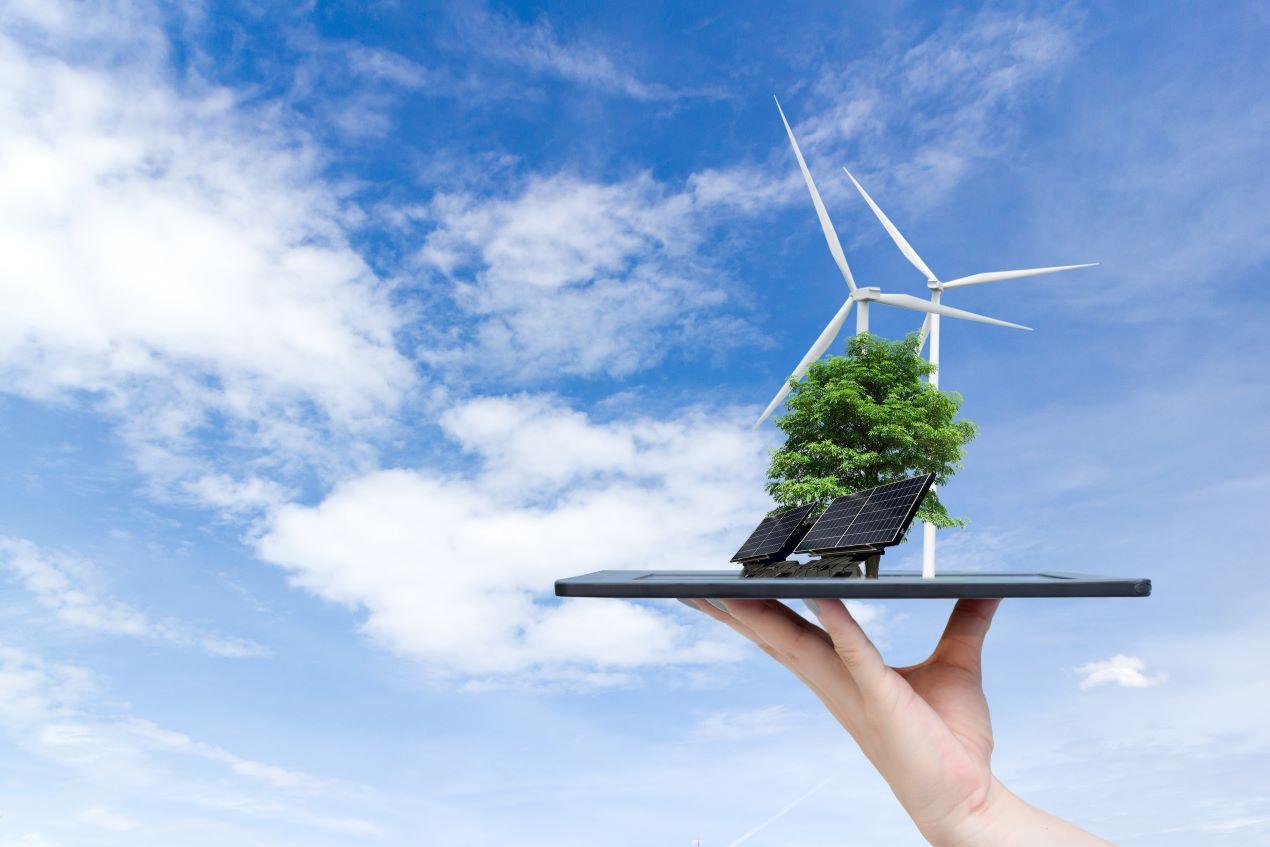 Darstellung eines nachhaltigen Energiesystems mit Solarzellen, einem Baum und einer Windkraftanlage auf einer Hand unter blauem Himmel.