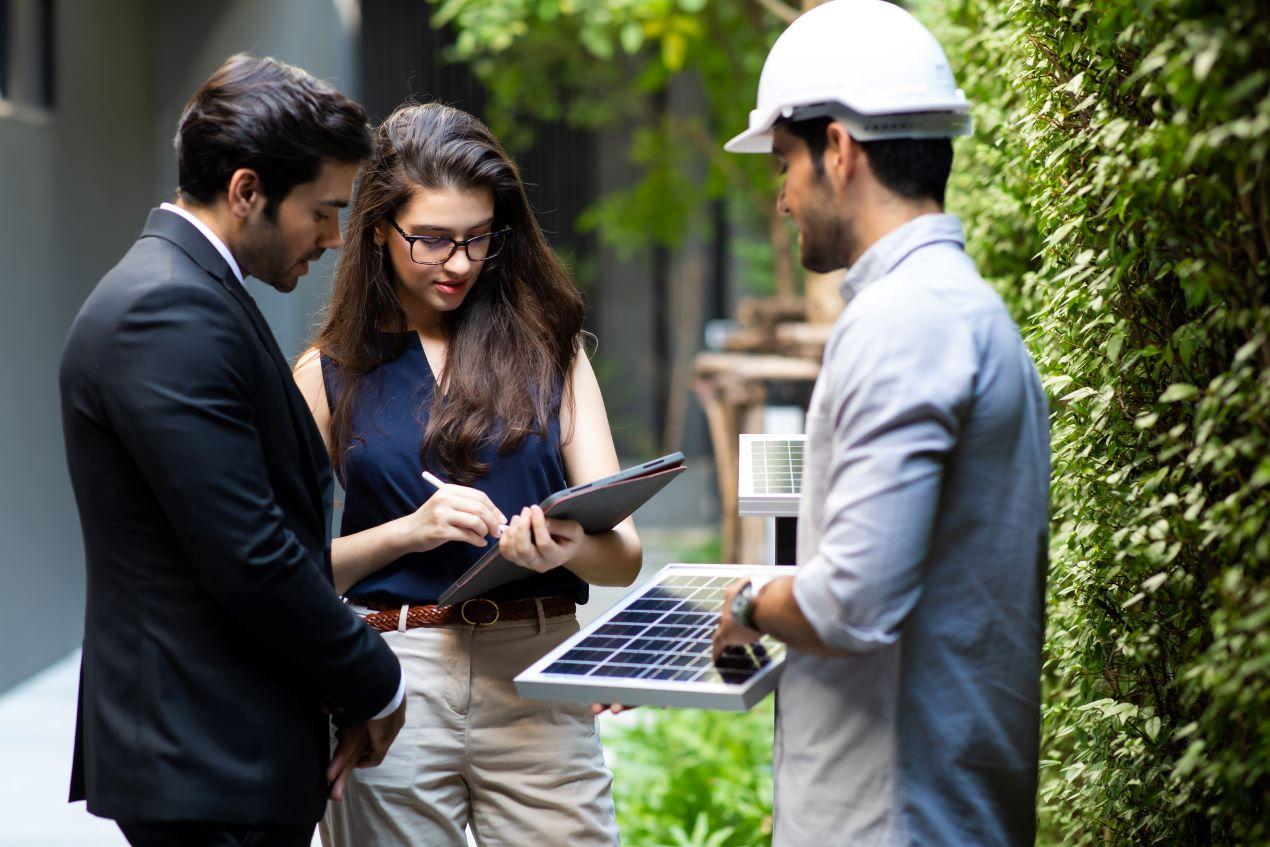 Ein Techniker erklärt einer Frau und einem Mann die Funktionsweise von Photovoltaikanlagen und dem Sunny Boy Storage mit einem Tablet und einer Mini-Solarplatte.